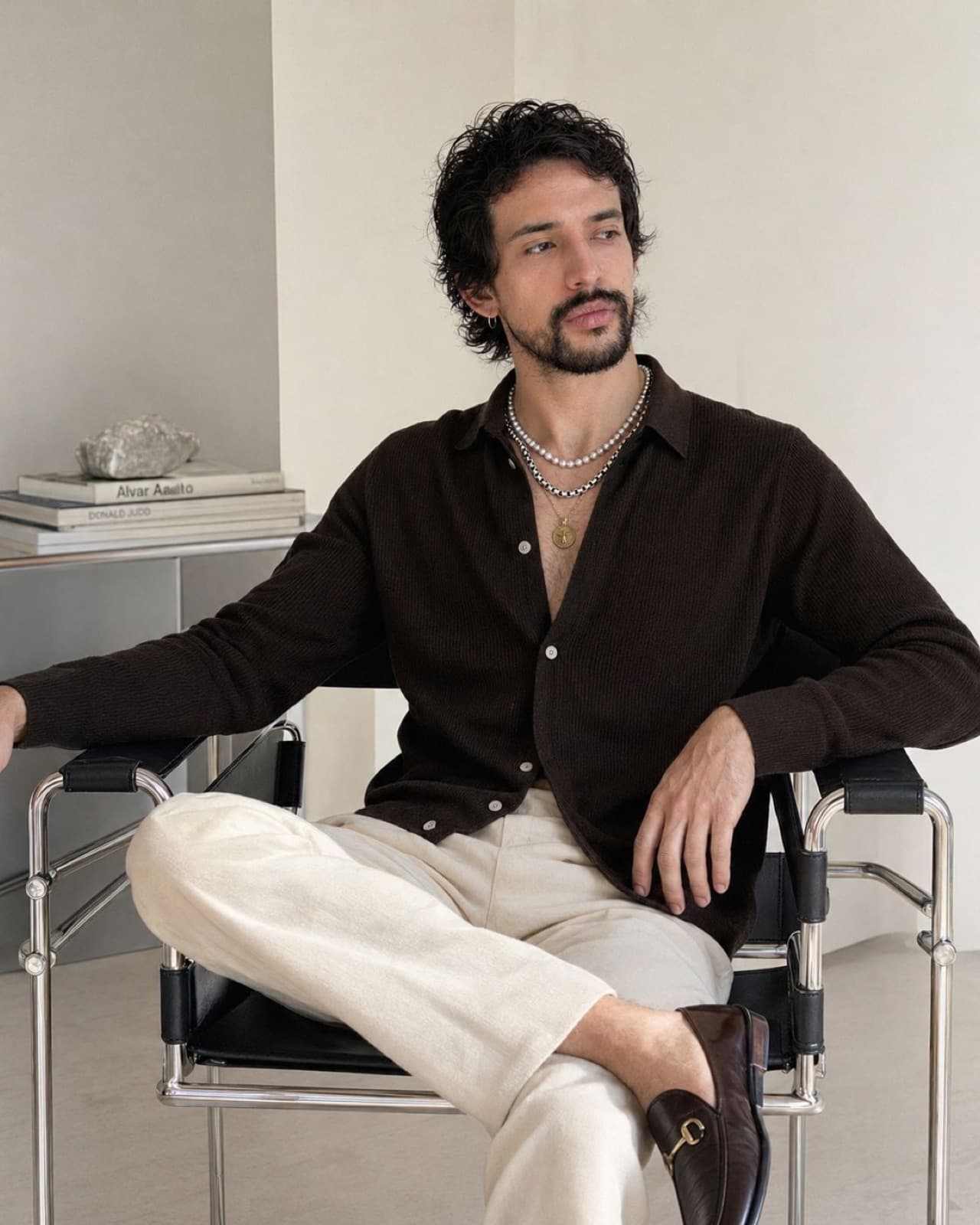 Alejandro del Palacio in a brown knit cardigan, seated in a modernist studio with architectural design books.
